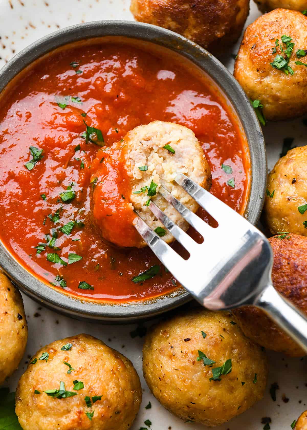 Chicken Meatballs being dipped into a bowl of marinara sauce with a fork
