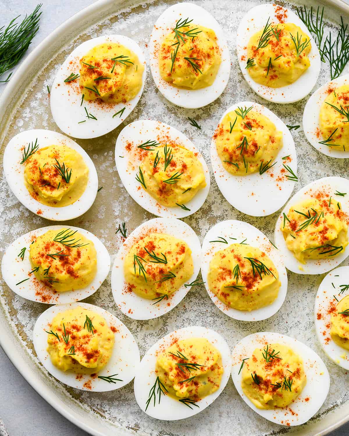 overhead photo of 14 Deviled Eggs on a platter garnished with dill and paprika
