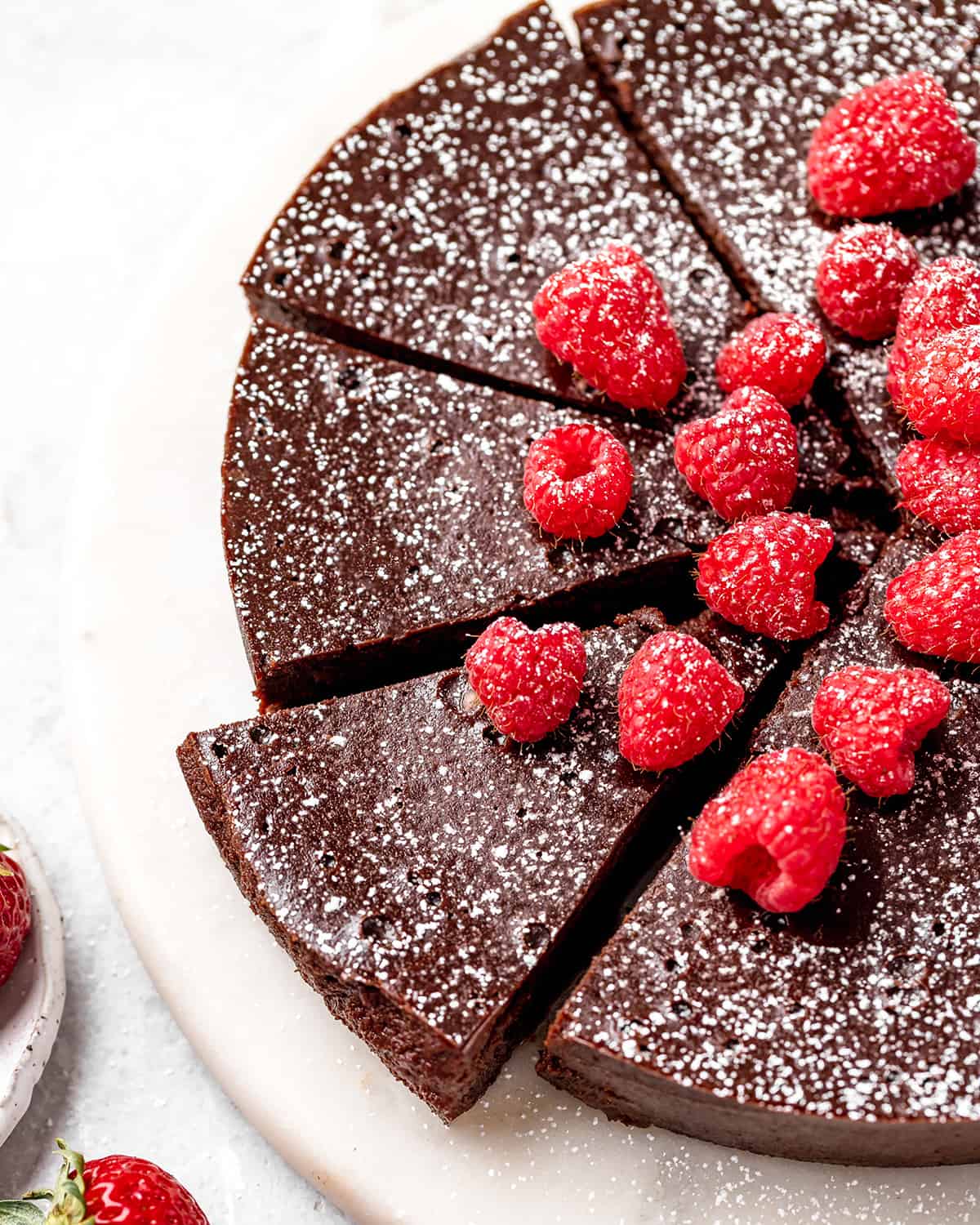 flourless chocolate cake with 4 slices cut topped with powdered sugar and raspberries