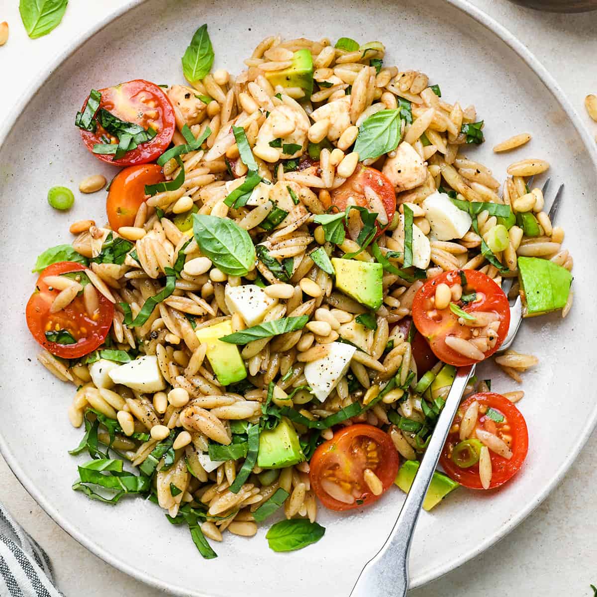 Caprese Orzo Salad on aplate garnished with pine nuts and avocado