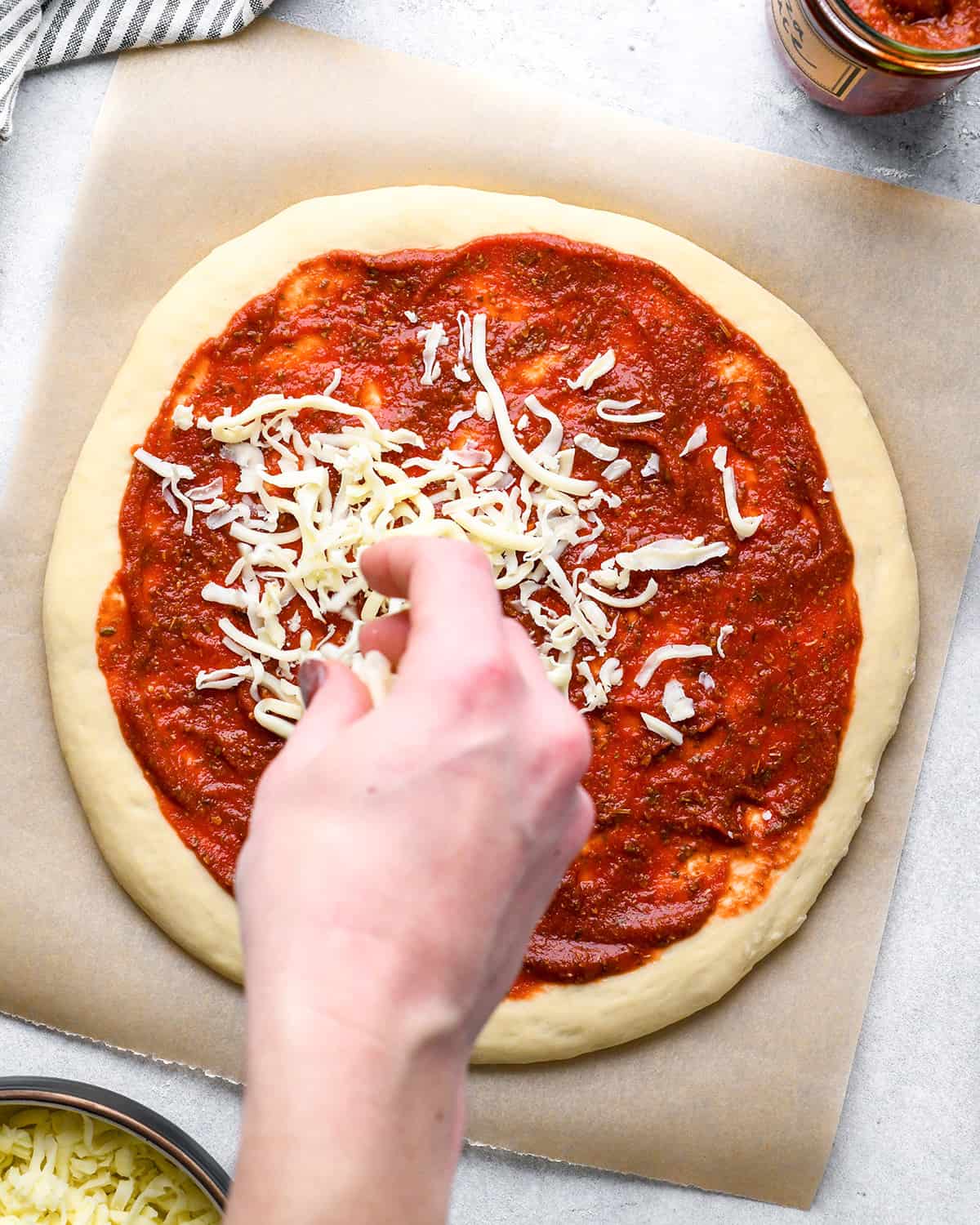 How to Make Pizza a hand sprinkling cheese over the sauce 
