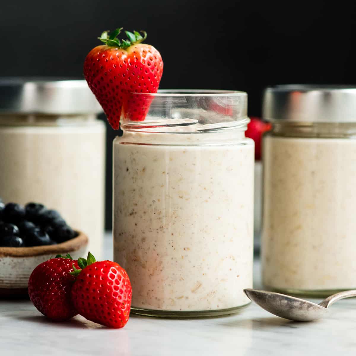 front view of three glass jars of Yogurt Overnight Oats with berries on top and around them
